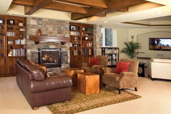 Traditional style living room with fireplace, bookcases, leather sofa and two upholstered armchairs after a basement remodel by B&B.